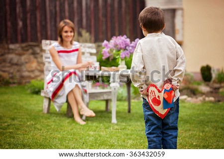 Beautiful mom, having coffee in a backyard, young cute child giving her present and flowers for her birthday. Mother day concept, love, happiness, cozy atmosphere