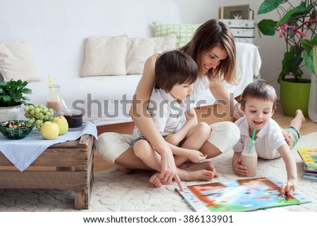 Young mother, read a book to her tho children, boys, in the living room, eating fruits and drinking smoothie, mothers day concept
