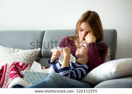 Young mother, holding her little sick boy, lying together on the couch