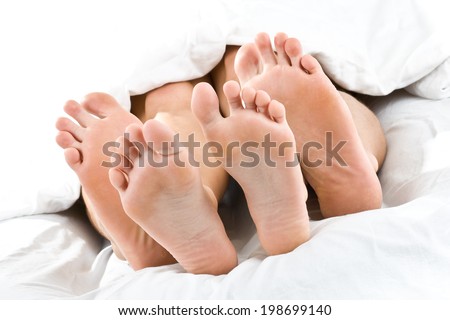 Four feet are lying upon each other under a blanket