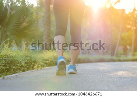 young fitness woman legs walking in the park outdoor, female runner running on the road outside, asian athlete jogging and exercise on footpath in sunlight morning. Sport,healthy and wellness concepts