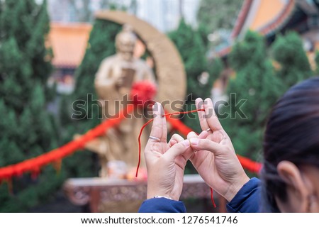 Young woman ties red rope and pray at Yue Lao (God of marriage) in Wong Tai Sin Temple, is well known for love and marriage prayers answered. landmark and popular for tourist attractions in Hong Kong
