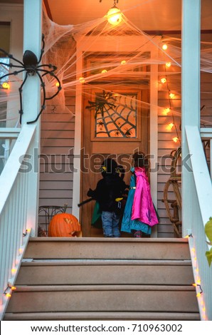 Children in Halloween costumes  knocking on door of decorated  neighborhood  fun trick or treat halloween night. Kids on Halloween trick or treat happy holiday.