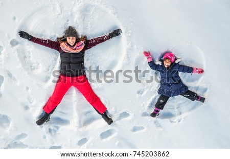 Happy family, mother and cute daughter making snow angel while lying on snow.