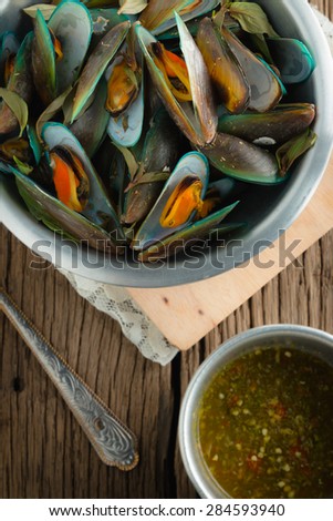 steam mussels with thai fresh herbs (basil, lemon grass, kaffir lime leaves) and seafood sauce on wooden background