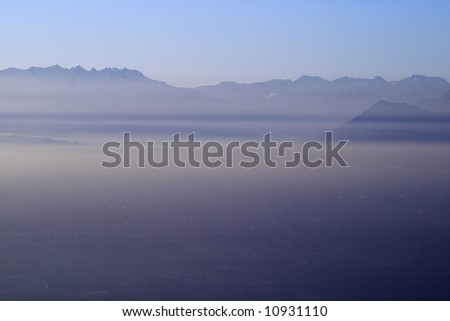 The city of Turin, Piedmont, Italy, lies hidden by dense smog and mist on a late winter afternoon. The peaks of the alps can be seen emerging from the mist in the background.