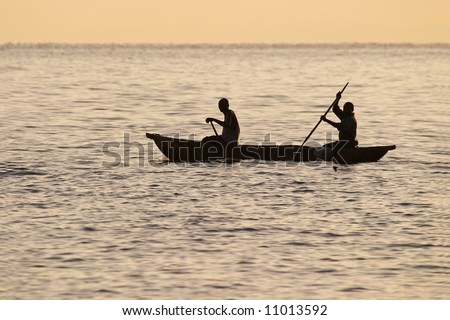 Two fishermen paddling a traditional bwato or dugout canoe past Makuzi Beach, malawi just after sunrise.