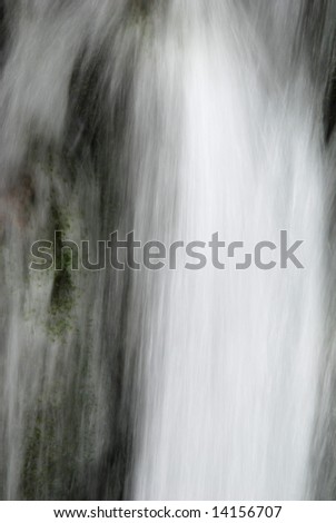 Abstract of fast moving water pouring over a mossy waterfall