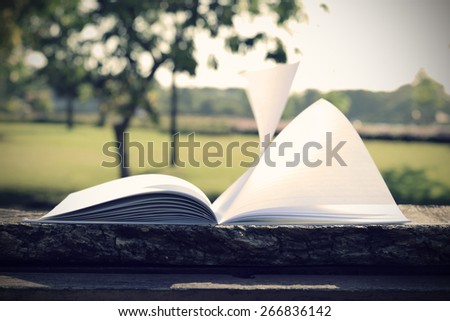 open book with flying book page on wood table (vintage background)