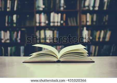 Close up of open book on desk and bookshelf with vintage filter blur background