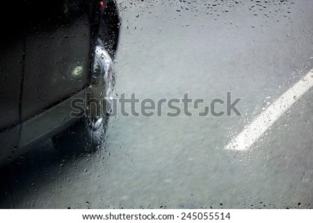 view of the road with the car through a window with raindrops