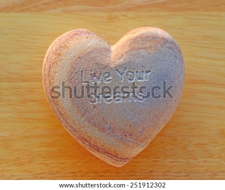 Natural stone in the shape of a heart with the inscription LIVE YOUR DREAMS  on the background of wood