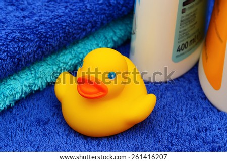 Yellow rubber duck in the background of two blue terry  towels and two white plastic bottles with yellow and blue label, close up