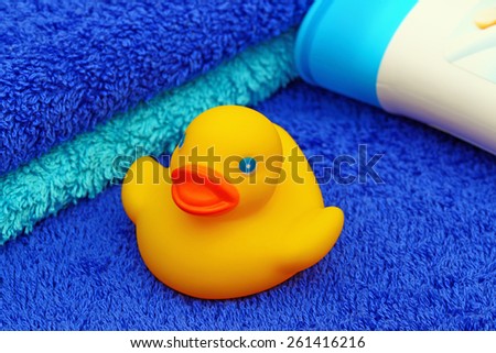 Yellow rubber duck in the background of two blue terry  towels and white plastic bottle with d blue cover