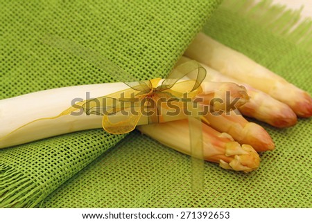 White fresh peeled asparagus with green and yellow bow on a background of four asparagus and green natural burlap fabric texture background