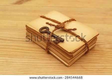 Tied with brown twine bundle of old yellowed paper with old rusty door key on wooden table background