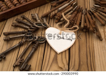 Life is Worth Living - hand-written text on a decorative white wooden heart, two round bunch of old metal rusty vintage door keys,  vintage brown wooden abacus on  old rustic wooden table background