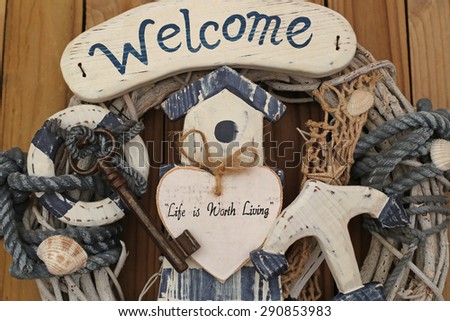 Welcome - Life is Worth Living - text on a decorative white wooden heart on maritime background, lighthouse, life buoy, door key, net, shells, marine rope, anchor, dry branches, close up, top view
