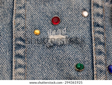 Close up of destroyed torn blue jeans  with orange thread seams and glass rhinestones