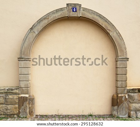 The walled up door with stone arch with metal rusty blue table with white number four on the ancient beige plastered walls background, photo frame, text place