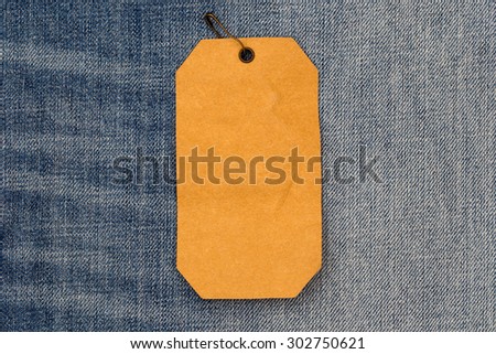 Close up of rumpled brown paper label  with brown pin on blue jeans background