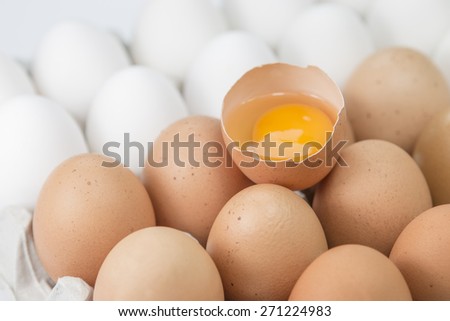 Broken egg in a cardboard with other brown and white eggs.