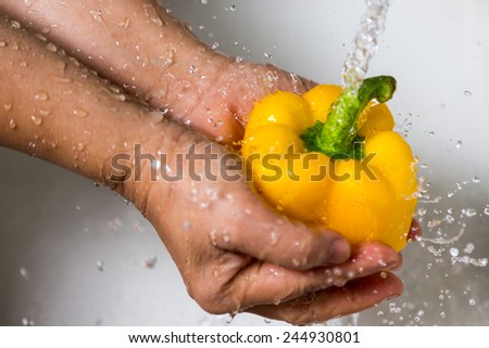 Female hands washing yellow pepper