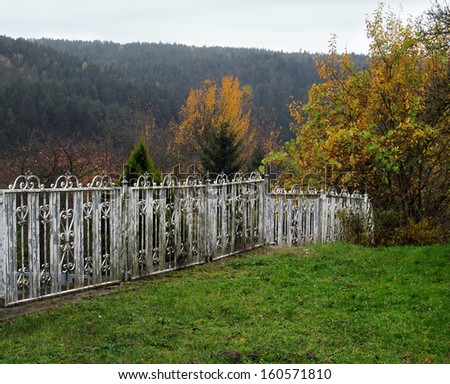 Autumn landscape with a white picket fence, hills and forests