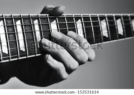 Man\'s hand holding vintage guitar fretboard and playing notes with fingers on strings.