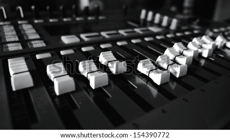 Mixing desk with faders and sliders in various positions mixing a track in low light giving a studio vibe.
