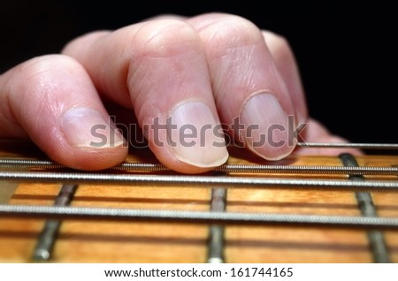 Fingers on bass guitar fretboard with guitar strings.