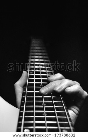 Playing guitar or bass with fingers on fretboard with dark background and copy space.