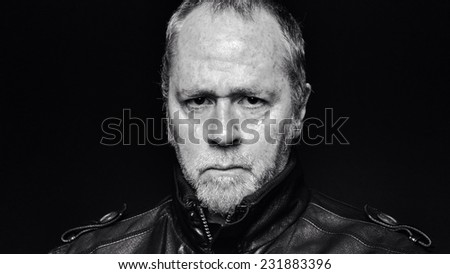 Tough, serious bearded man in leather jacket on black background (black and white).