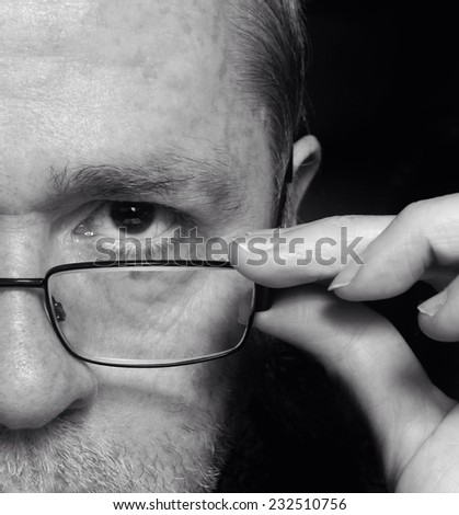Curious, questioning or inquisitive man peering over glasses or spectacles on black background.