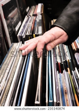 Man in leather jacket searching and browsing through vinyl albums at a record store.