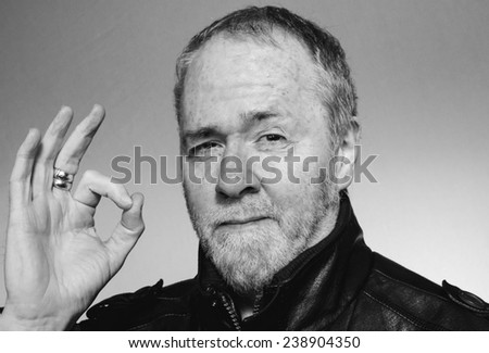 Man with stubble and motorcycle jacket giving the OK sign with his fingers and winking.