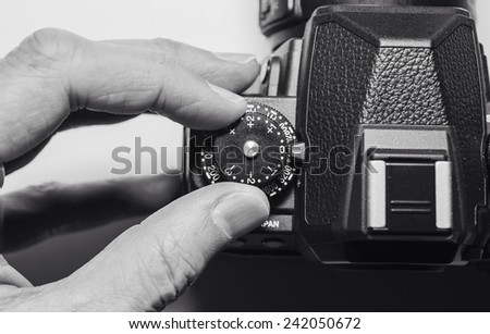Taking a photograph with fingers changing controls and dials on a digital camera or DSLR.