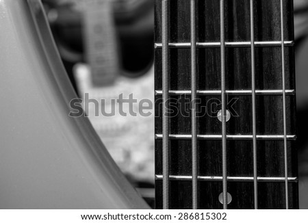 Bass guitar neck and strings in extreme close up with 6-string electric guitar visible in background.