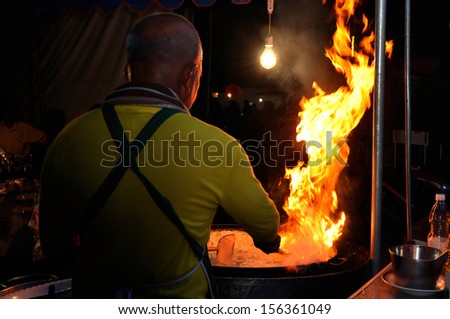 Chef cook making a show with flames while cooking in a night market.