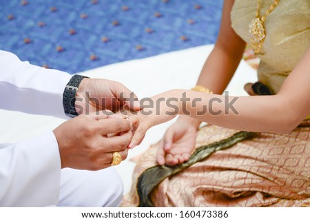 Groom places a diamond ring onto the brides hand during a wedding ceremony