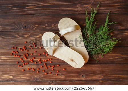 Hand-made wooden slippers for sauna, Russian baths or spa with red mountain ash or rowan berries on rustic wooden background