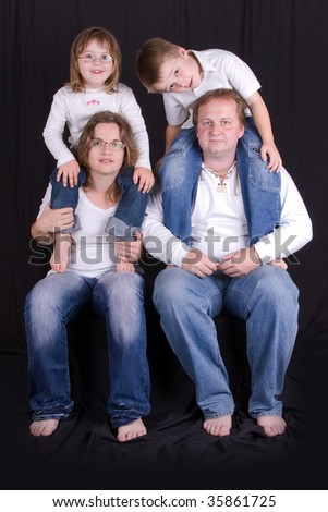 Happy young family - mother, father, daughter and son - black background - studio photo