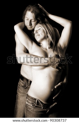 Portrait of a happy young couple, holding each other lovely and touching her belly together while making fun to each other. They are smiling because they expecting a baby, image on black background