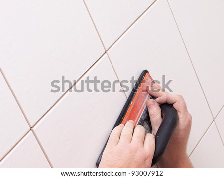 Hands grouting a ceramic tile floor or wall using a rubber float