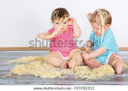 Messy baby toddlers having fun eating pasta