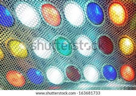 Image of red, yellow, blue, white and green spot lights behind metal grid with hexagonal cells