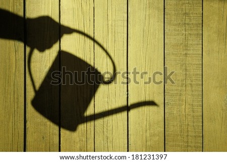 Shadow of watering can on natural wooden background, with space for text or image.