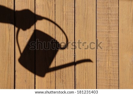 Shadow of watering can on natural wooden background, with space for text or image.