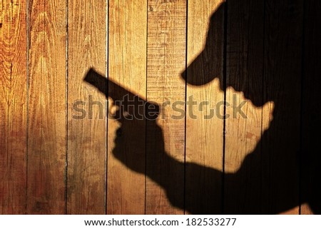 Man in silhouette with gun ready to shoot on natural wooden background, with space for text or image.