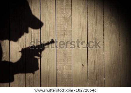 Human silhouette with handgun in shadow on wood background, with space for text or image.